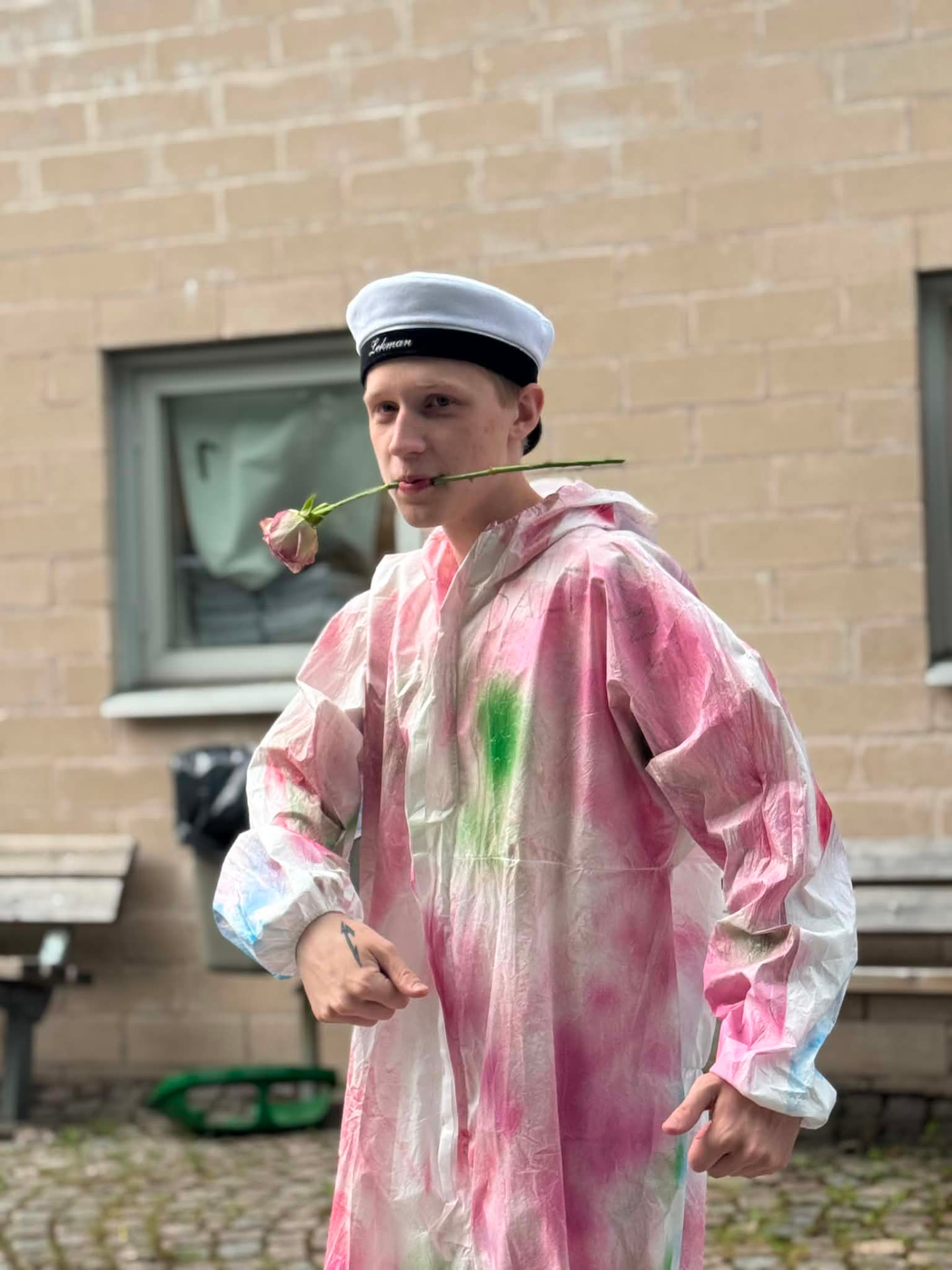 Nathan i färgglad regnrock med en ros i munnen på studentdagen